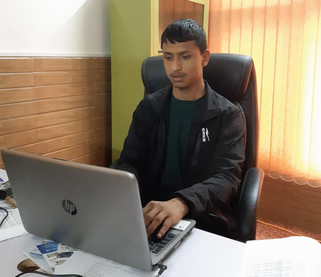 A person wearing green t-shirt and black jacket working in his laptop