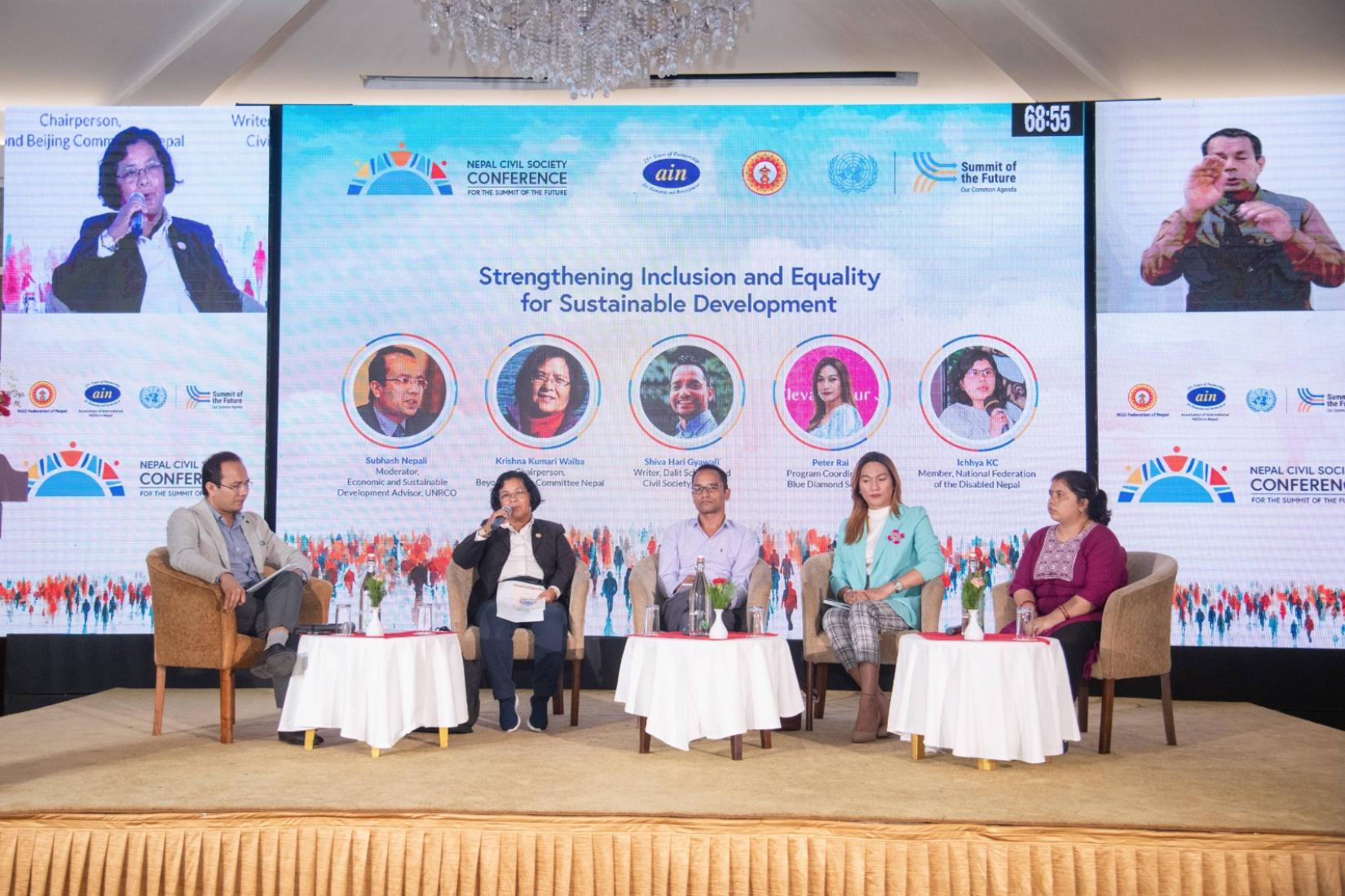 Panel discussion with five speakers on stage, with a banner in the background and a large screen showing a speaker and a sign language interpreter. The banner title reads: Strengthening Inclusion and Equality for sustainable development. 