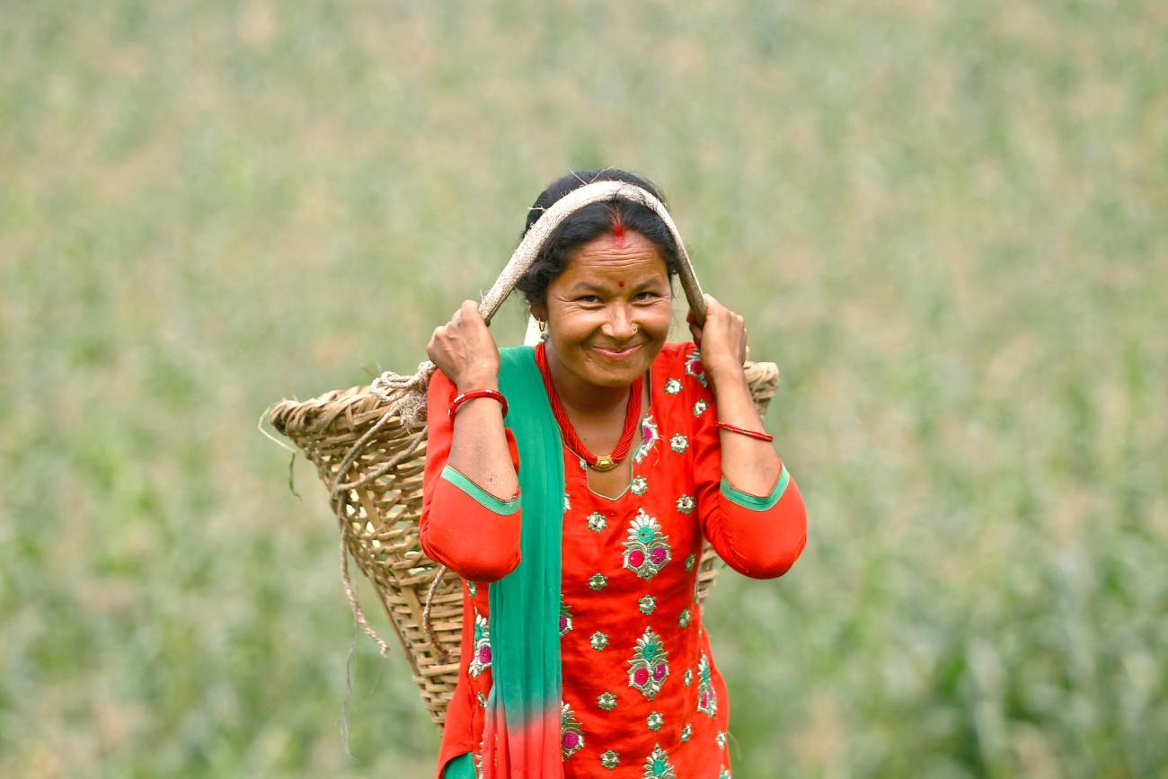 A woman in red kurtha surwal is carrying a traditional bucket (Doko)