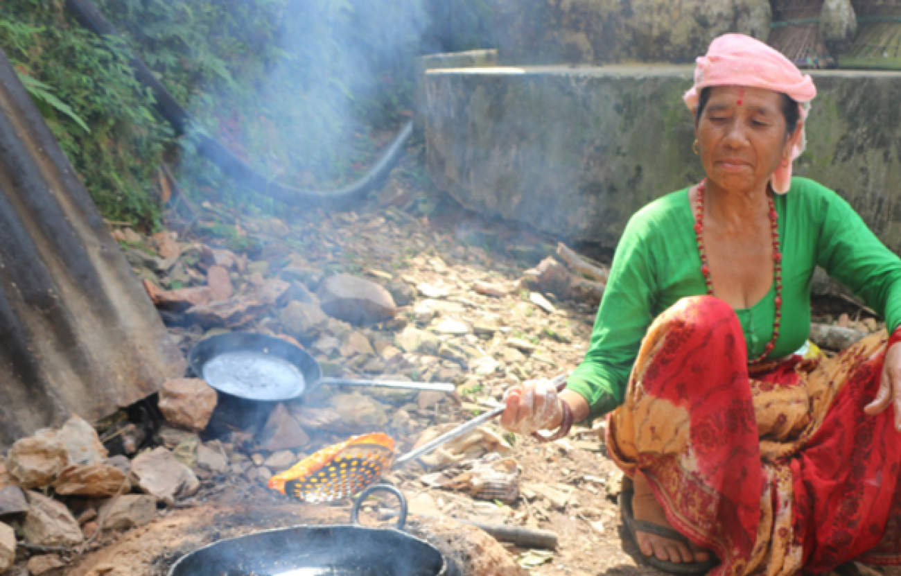An old Woman with green blouse and red saree making Papad in a black pot filled with oil outside on the ground.