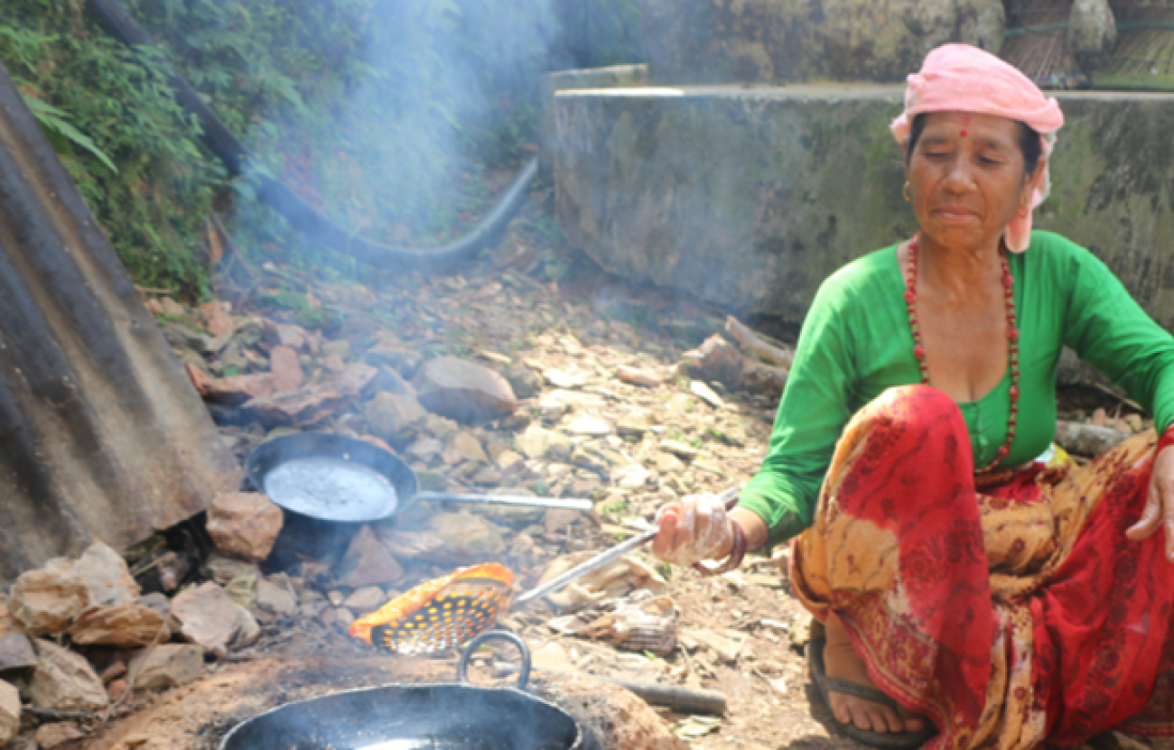 An old Woman with green blouse and red saree making Papad in a black pot filled with oil outside on the ground. 