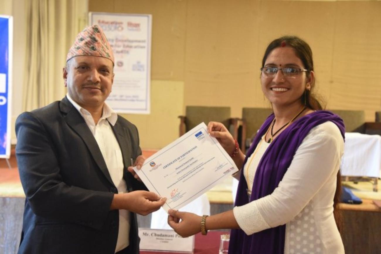 A woman wearing white kurtha and purple shawl receives a certificate from a guy wearing dhaka topi and a black coat. 
