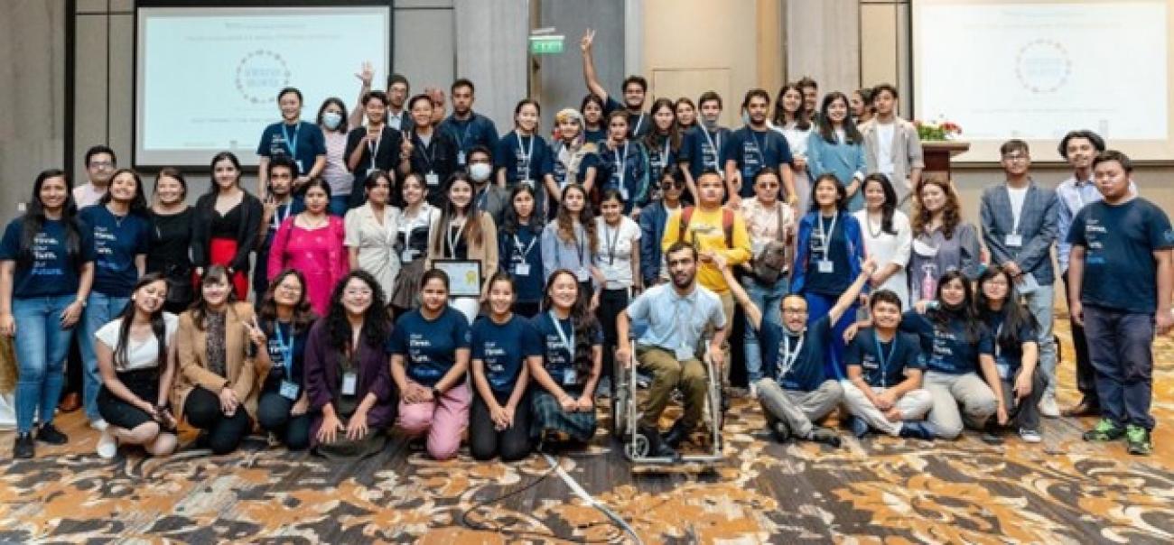 A group of around 70 UN youth volunteers, most wearing matching navy blue T-shirts, posing in a conference room