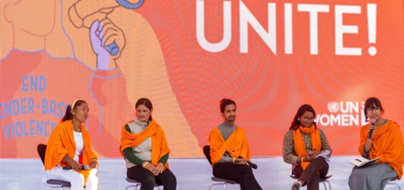 Five filmmakers are sitting in a chair on stage with an orange scarf around them