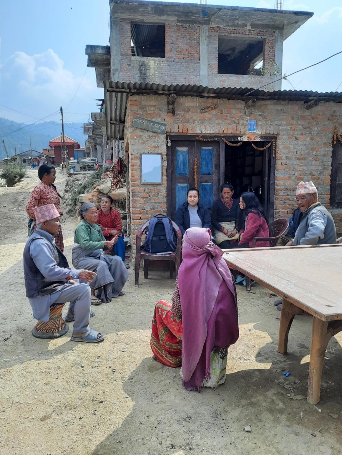 A group of around nine people sit outside a newly constructed house and have a discussion.  Assessment for persons with severe mental health condition at Lele, Godawari, Province Bagmati, Nepal; Photo Credit: KOSHISH