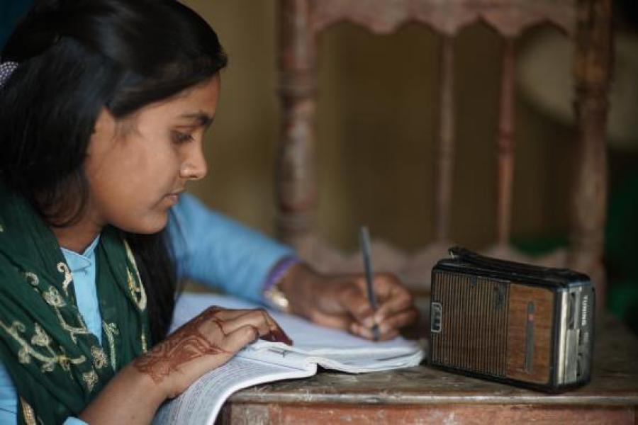 Sakila Khatun, 13, listens to the radio in her home in Parsa District in southern Nepal as she finishes up her homework.
