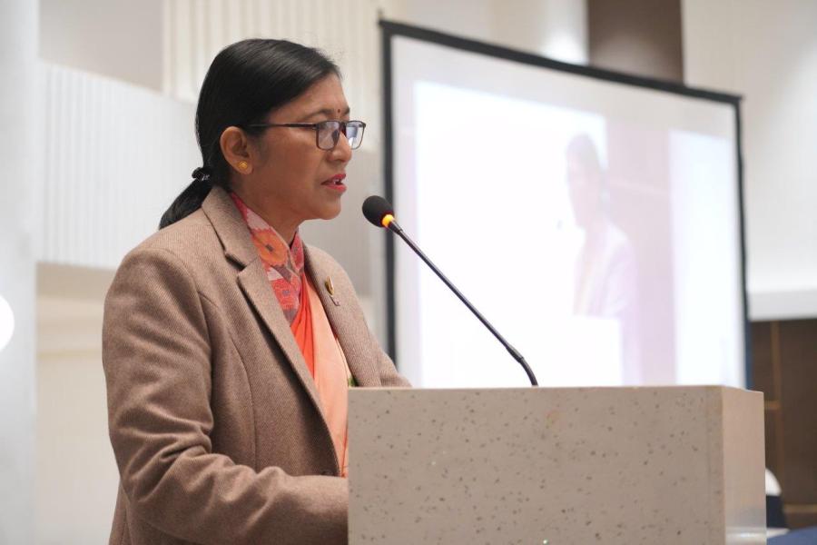 Honorable Dr. Janaki Kumari Tuladhar, Commissioner, Election Commission Nepal sharing the lessons from the 2022 elections. She is wearing pink saree, brown coat and standing in front of podium.