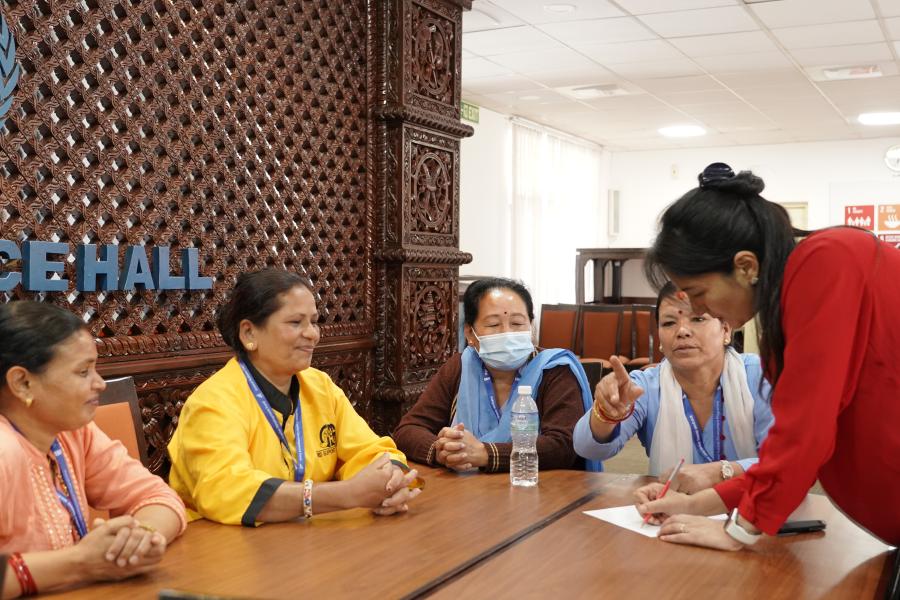 A group of women are discussing and sharing their perspective to their group member who is standing and writing down all the notes that are being provided to her.