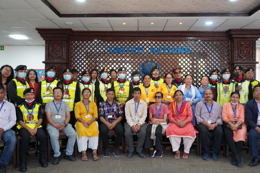 A group picture of the staff members who participated in the disability and inclusion pilot project in the conference hall. In the background is a logo of the United Nations, with people in the front row sitting and the second row standing.