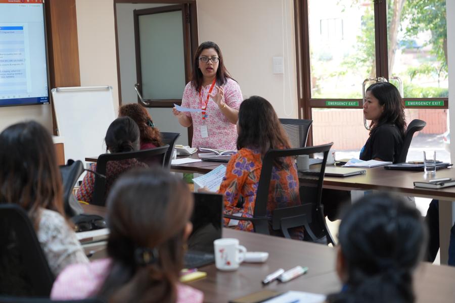 A participant wearing pink and white Kurtha is standing with her notes in hand. She is presenting the key points discussed with her group members to rest of the participants regarding PSEA in the conference room.