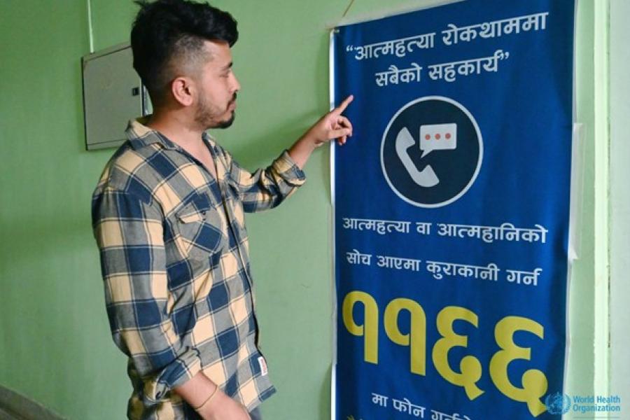 Man wearing blue and yellow checkered shirt reads a poster in front of him that gives information on helpline number for suicide prevention.