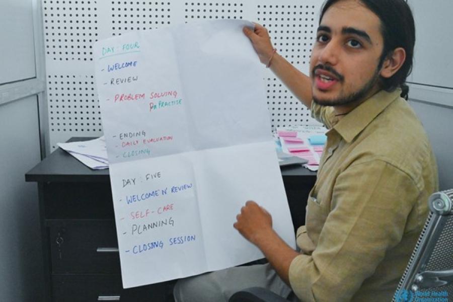 A counsellor at the Suicide Prevention A counselor wearing khaki shirt and grey pants turns around from his desk holding a chart paper.