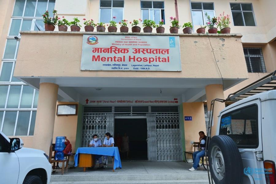 Main entrance of the mental hospital. the yellow building has a big board right in the middle of the building with the name, location and other information written on it.