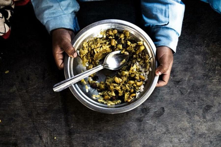 A child's hand holding a steel plate filled with black eyed beans and rice with a spoon.