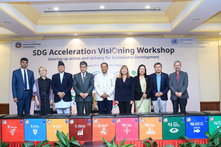four panelists of the event as well as Toya Narayan, Hanaa Singer and Min Bahadur stands on stage with a big colorful banner behind and SDG blocks in the front.  