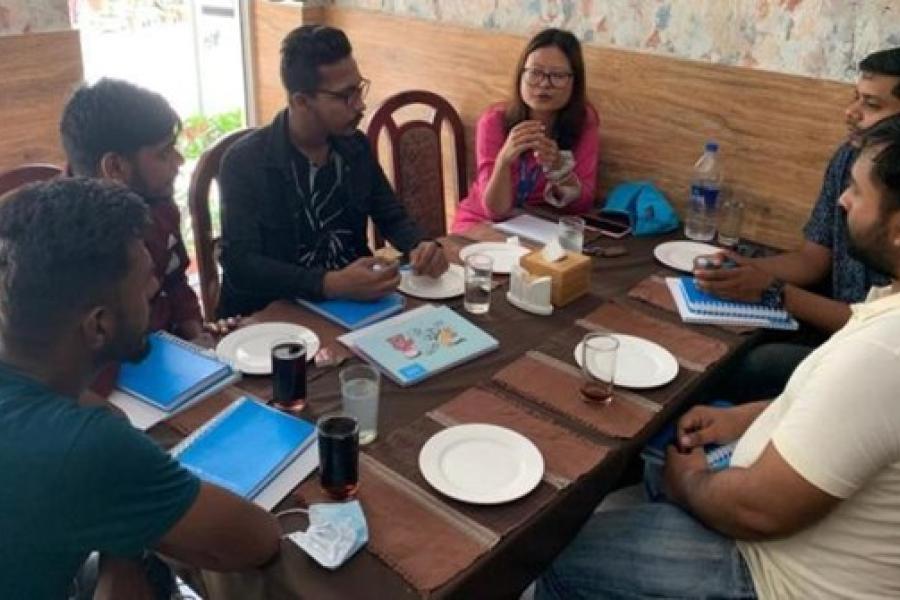 Six people (one woman, five men) sitting around a table with notebooks, water and Coca-Cola, having a discussion.