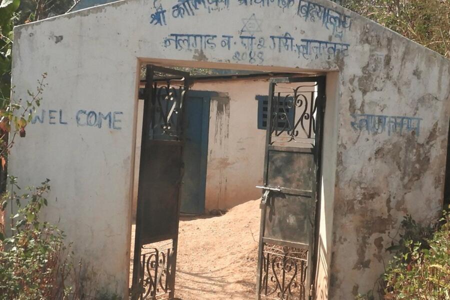 A blue gate is attached with a white wall with name of the school and welcome written on it.