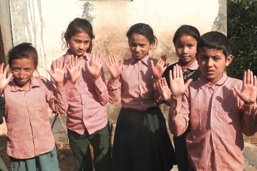 Five school children have their hands in front of them showing their palm. They wearing their red and whited checkered school uniform.