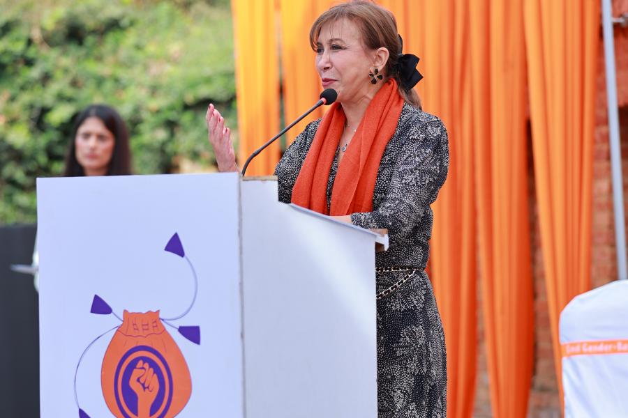 UN Nepal Resident Coordinator speaking into a podium microphone with orange drapes in the background