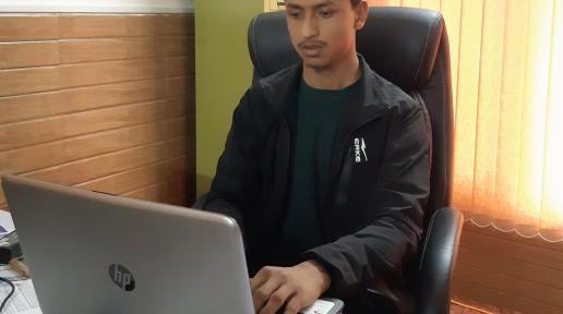 A person wearing green t-shirt and black jacket working in his laptop