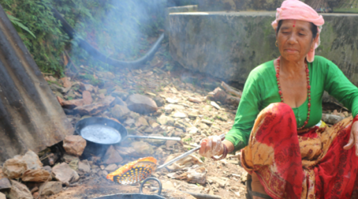 An old Woman with green blouse and red saree making Papad in a black pot filled with oil outside on the ground. 