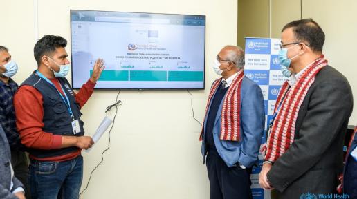 A man points at the tv screen explaining two other men standing in front of him at the teleconsultation center.