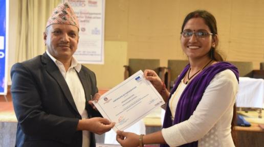 A woman wearing white kurtha and purple shawl receives a certificate from a guy wearing dhaka topi and a black coat. 