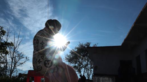 A woman is sitting on a chair outdoors, looking at her phone.
