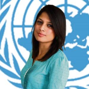 Profile photo of Simrika, RCO. Woman with dark hair and a blue blouse in front of the UN symbol.