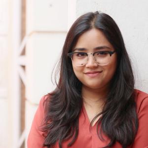 A girl wearing red t-shirt and glasses is posing for a picture with a smile on her face.